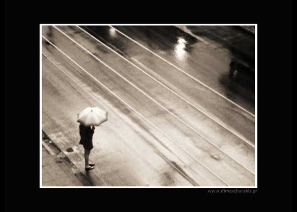 γυναίκα ντυμένη στα μαύρα κρατάει ομπρέλα στην άκρη ενός δρόμου