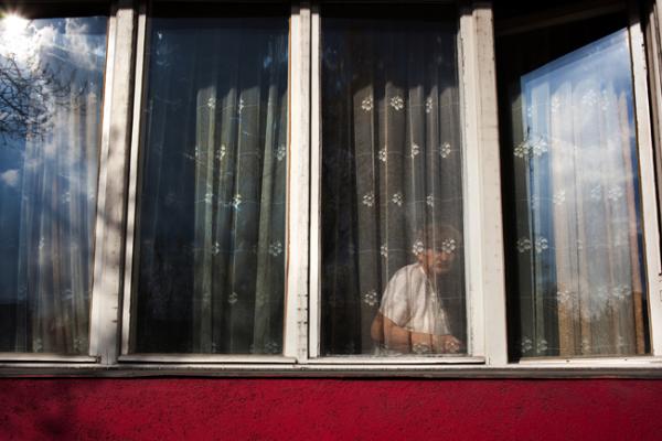 ηλικιωμένη γυναίκα κοιτάζει μέσα από το παράθυρο του σπιτιού της