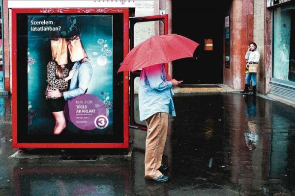 street photography, άντρας κρατάει κόκκινη ομπρέλα μπροστα από αφίσα που δείχνει ζευγάρι με σακούλες στα κεφάλια