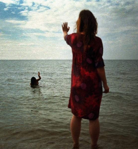 γυναίκα στην παραλία χαιρετά μία άλλη γυναίκα μεσα στη θάλασσα