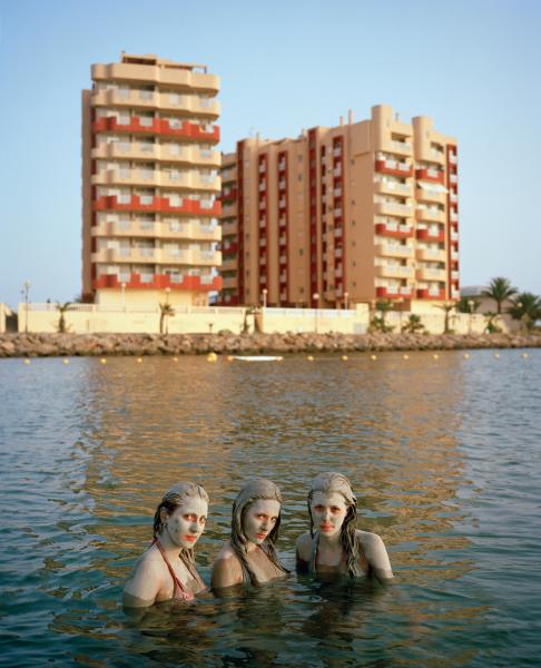 γυναίκες με λάσπη στο πρόσωπο ποζάρουν μεσα σε θάλασσα, μπροστά απο κτήρια