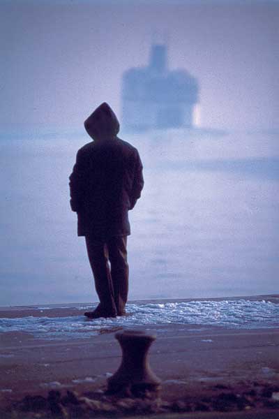 άντρας περιμένει στο λιμάνι, πλοίο στο βάθος