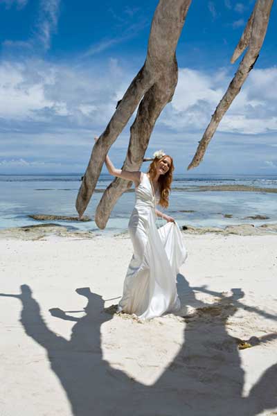 γυναίκα με μακρύ άσπρο φόρεμα ποζάρει σε μία παραλία