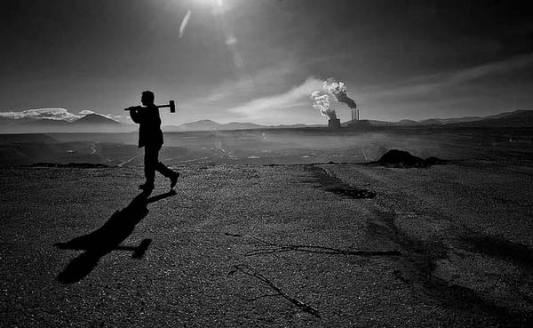 ασπρόμαυρη φωτογραφία, εργάτης περπατάει, στο βάθος το εργοστάσιο της ΔΕΗ στη Κοζάνη