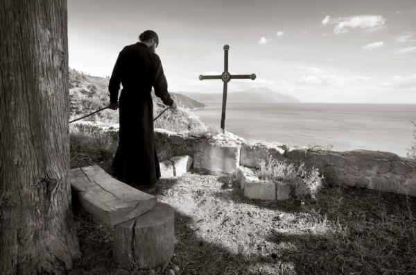 μοναχός στο άγιο όρος πίσω απο έναν σταυρό με θέα την θάλασσα