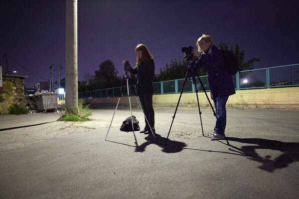 δύο κοπέλες με φωτογραφικές μηχανές στημένες σε τρίποδα φωτογραφίζουν στη νύχτα