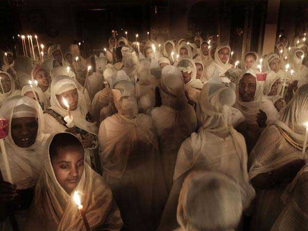 πιστοί σε ιερό ναό με λευκά κεριά και λευκά ρούχα