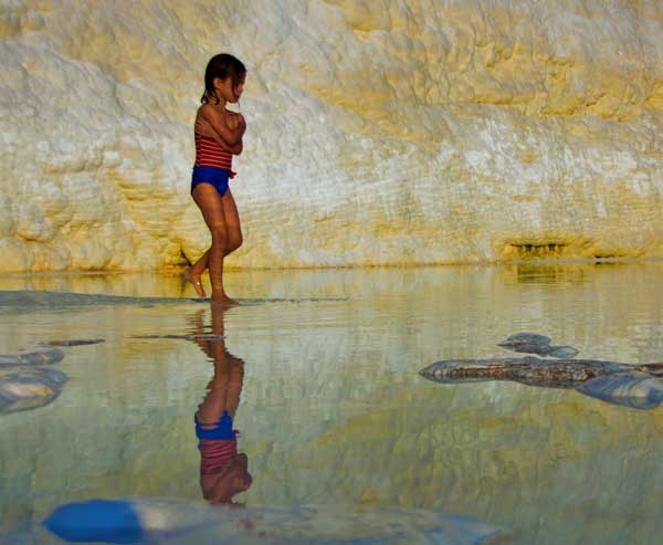 παιδί περπατάει σε κάποια παραλία, από πίσω του ένας βράχος