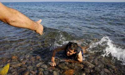 ένας άνδρας βοηθάει έναν πρόσφυγα να βγεί στην στεριά