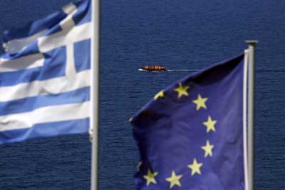 μία λέμβος φαίνεται στη θάλασσα ανάμεσα απο τις σημαίες της Ελλάδας και της ΕυρωπαΪκής Ένωσης