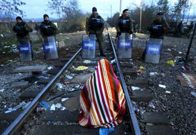 μία γυναίκα κάθεται πάνω στις γράμμες τρένου μπροστά σε αστυνομικούς στα σύνορα ΠΓΔΜ