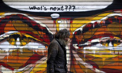 ένας άνδρας περπατά μπροστά απο ένα γκράφιτι που λέει What's next???