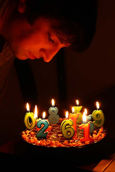 άνδρας σκύβει πάνω από μία τούρτα γενεθλίων με πολλά κεράκια - αριθμούς