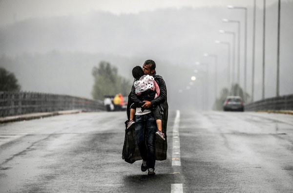 πρόσφυγας στη βροχή κρατάει στην αγκαλιά του το παιδί του