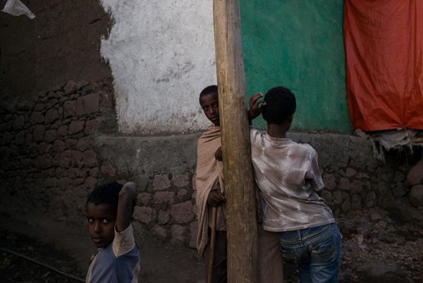 τρία αγόρια από την Αιθιοπία, το ένα γυρισμένο πλάτη σε μια ξύλινη κολώνα