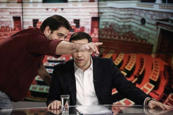 ο Αλέξης Τσίπρας σε τηλεοπτικό στούντιο και δημοσιογράφος του κρύβει το πρόσωπο δείχνοντας του με το χέρι σηκωμένο προς την κάμερα