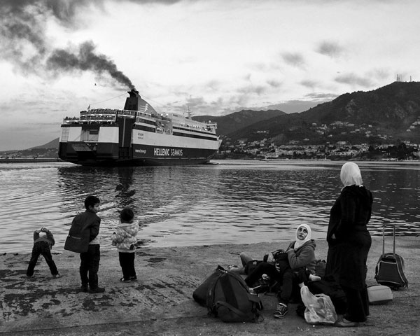 Συριακή οικογένεια κοιτάζει πλοίο που φεύγει από το λιμάνι της Λέσβου, περιμένοντας να επιβιβαστεί σε ένα από τα επόμενα για το λιμάνι του Πειραιά. 2015