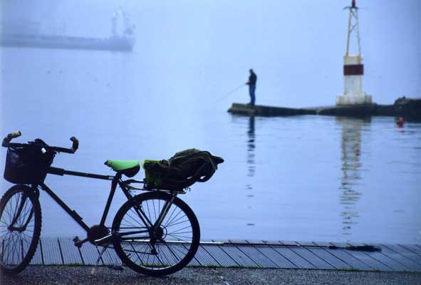ποδήλατο σε λιμάνι με φόντο ένα ψαρά και ένα φάρο