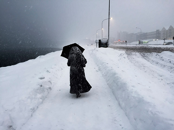 γυναίκα ντυμένη στα μαύτα περπατάει σε χιονισμένο δρόμο