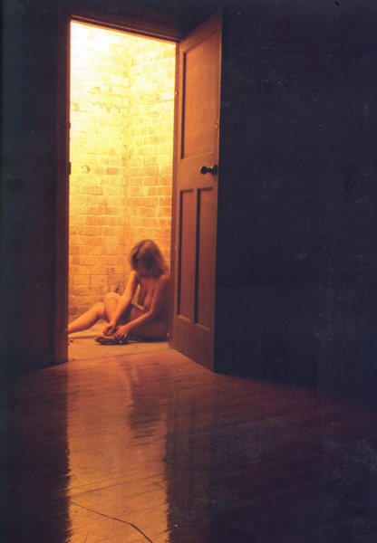 Ενότητα 2 φωτογραφιών-τεκμηρίωση της περφόρμανς “Charlie” / γυμνή γυναίκα κάθεται στο πάτωμα δίπλα σε ανοιχτή πόρτα
