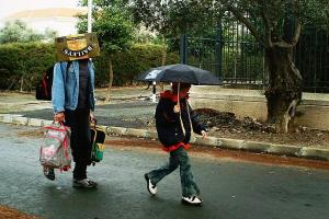 άντρας περπατάει στη βροχή κρατώντας δύο σχολικές τσάνες και με ενα χαρτοκούτι στο κεφάλι / παιδί περπατάει στη βροχή κρατώντας ομπρέλα