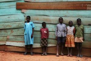 παιδάκια της Αφρικής ποζάρουν όρθια σε έναν πράσινο ξύλινο τοίχου σπιτιού