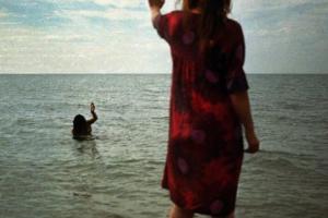 γυναίκα στην παραλία χαιρετά μία άλλη γυναίκα μεσα στη θάλασσα