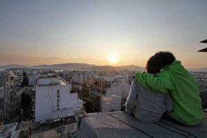 δύο παιδιά αγκαλιασμένα, ανεβασμένα σε κτήριο κοιτάνε το ηλιοβασίλεμα