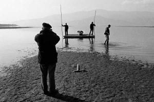 ασπρόμαυρη φωτογραφία / ένας άνδρας κοιτά τρείς άνδρες μέσα σε μία λίμνη