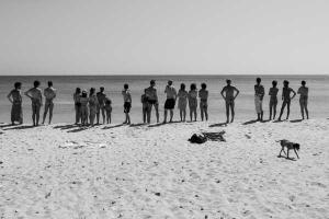 ασπρόμαυρη φωτογραφία ανθρώπων που στέκονται σε μία παραλία κοιτώντας τη θάλασσα άλλοι με μαγιό και άλλοι γυμνοί
