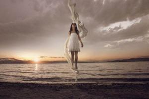 κορίτσι με λευκό φόρεμα ίπταται πάνω από τη θάλασσα την ώρα που δύει ο ήλιος