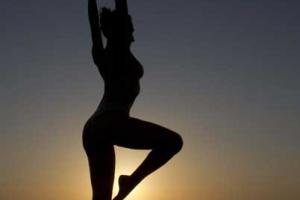 γυναίκα γυμνή σε όρθια στάση με λυγισμένο το γόνατο / απο πίσω θάλασσα και ηλιοβασίλεμα