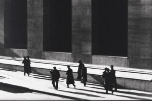 ασπρόμαυρη φωτογραφία, άνδρες ντυμένι στα μαύρα περπατάνε σε προαύλιο χώρο δημόσιου κτηρίου