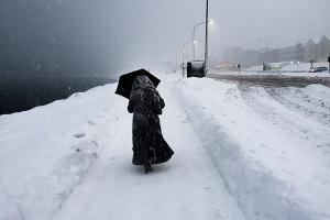 γυναίκα ντυμένη στα μαύτα περπατάει σε χιονισμένο δρόμο